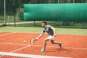 uomo giocando tennis. fiducioso giovane uomo nel gli sport Abiti giocando tennis su tennis Tribunale foto