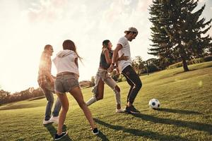 giocando difficile. pieno lunghezza di giovane persone nel casuale indossare in esecuzione mentre giocando calcio all'aperto foto