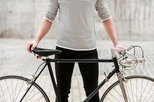 orgoglioso di il suo bicicletta. avvicinamento di giovane uomo Tenere mani su il suo bicicletta mentre in piedi all'aperto foto