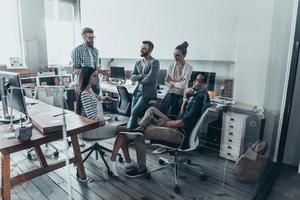 squadra di giovane professionisti. bello giovane uomo nel casuale indossare e occhiali conduzione Presto attività commerciale incontro mentre il suo squadra ascoltando per lui foto