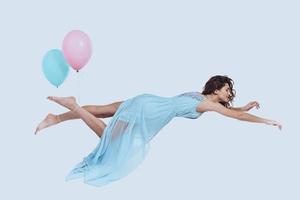 sognare volare. studio tiro di attraente giovane donna nel elegante vestito conservazione braccia disteso mentre librarsi contro grigio sfondo foto