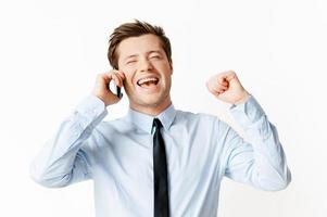 grande notizia contento giovane uomo nel camicia e cravatta parlando su il mobile Telefono e Esprimere a gesti mentre in piedi isolato su bianca foto