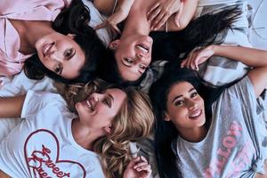 semplicemente sbalorditivo. superiore Visualizza di quattro attraente giovane donne nel pigiama sorridente mentre dire bugie su il letto a casa foto