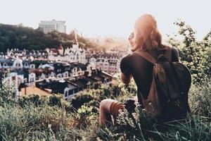 bellissimo Visualizza. posteriore Visualizza di giovane uomo nel casuale capi di abbigliamento Fotografare il Visualizza mentre seduta su il collina all'aperto foto