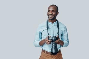 bello giovane africano uomo guardare lontano e sorridente mentre in piedi contro grigio sfondo foto