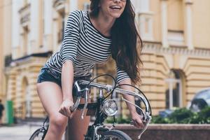 equitazione con divertimento. avvicinamento di bellissimo giovane donna equitazione bicicletta lungo il strada e sorridente foto