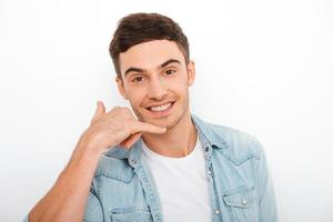 chiamata me qualunque tempo contento giovane uomo Esprimere a gesti e sorridente mentre in piedi contro bianca sfondo foto