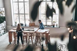 analizzando dati. superiore Visualizza di giovane colleghi nel inteligente casuale indossare utilizzando planimetria mentre Lavorando nel il creativo Lavorando spazio foto