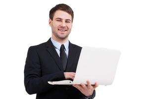 uomo d'affari con il computer portatile. allegro giovane uomo nel vestito formale Lavorando su il computer portatile e sorridente mentre in piedi isolato su bianca foto