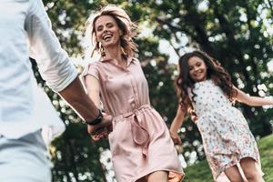 vero gioia di appena essere intorno a. contento giovane famiglia di tre Tenere mani e sorridente mentre in esecuzione nel parco foto