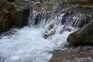 avvicinamento Immagine di un' piccolo selvaggio cascata nel il modulo di corto flussi di acqua fra montagna pietre foto