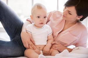 madre amore. bellissimo giovane madre dire bugie su lato nel letto mentre poco bambino seduta vicino per sua foto