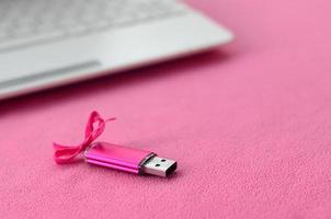 brillante rosa USB veloce memoria carta con un' rosa arco bugie su un' coperta di morbido e peloso leggero rosa vello tessuto accanto per un' bianca il computer portatile. classico femmina regalo design per un' memoria carta foto