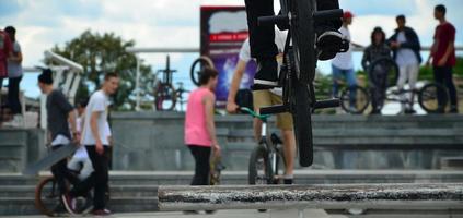 un' ciclista salti al di sopra di un' tubo su un' bmx bicicletta. un' lotto di persone con biciclette nel il sfondo. estremo gli sport concetto foto