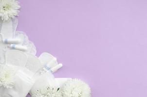 mestruale pastiglie e tamponi con tenero bianca fiori su pastello lilla sfondo foto