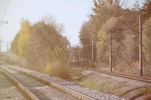 autunno industriale paesaggio. ferrovia sfuggente in il distanza tra verde e giallo autunno alberi foto