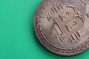 cioccolato Prodotto nel il modulo di fisico bitcoin bugie su un' verde plastica sfondo. modello di il crypto moneta nel il commestibile modulo foto