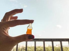 marmellata caramelle. un' ragazza con un' rosso manicure detiene dolci nel il forma di un' bottiglia con limonata. caramelle su un' sfondo di blu cielo. acquolina in bocca dolci foto