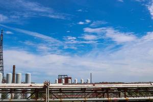 Visualizza di un' tubatura cavalcavia con tubi, colonne di carri armati contro un' blu cielo con nuvole a un industriale chimico raffineria prodotto petrochimico pianta