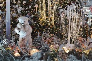 negozio finestra decorazione, shopping centro arredamento. artificiale bianca abete rosso con ghirlande. Il prossimo per loro è un' giocattolo orso con un' orsacchiotto orso nel sua braccia. giocattolo decorazioni con mobile meccanismi foto