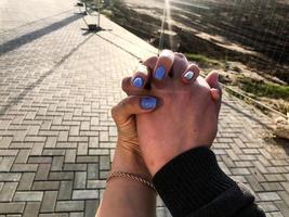 ragazza e tipo hold mani. il ragazze Chiodi siamo coperto con blu-argento vernice. bellissimo e elegante manicure. amore fra un' uomo e un' donna. contro il sfondo di asfalto foto