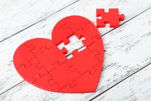 cuore puzzle rosso su fondo di legno bianco