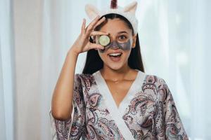 divertente sorridente terme donna con fresco facciale maschera hold cetriolo. foto