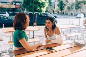 Due bella amiche parlando mentre seduta nel un' bar all'aperto foto