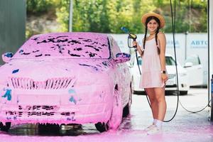 donna con tubo flessibile sta di auto coperto nel rosa schiuma foto