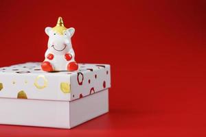 unicorno figurina su un' regalo scatola su un' rosso sfondo con gratuito spazio. foto