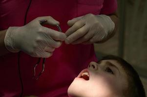 il pediatrico dentista ossequi il del bambino denti, spazzolatura il dente a partire dal carie con un' trapano. foto