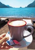 tazza di caffè su il spiaggia vicino il mare nel soleggiato giorno foto