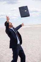 io am gratuito fiducioso giovane uomo nel vestito formale Lavorando su digitale tavoletta e sorridente mentre in piedi nel deserto foto