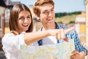 Guarda al di sopra di Là contento giovane turista coppia Tenere carta geografica mentre donna puntamento lontano e sorridente foto