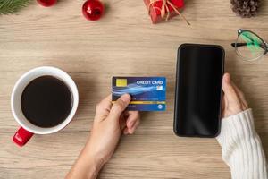 mano Tenere credito carta per in linea shopping su smartphone durante potabile caffè. allegro Natale vigilia, dicembre, di stagione, nero Venerdì saldi, nuovo anno e vacanza concetto foto