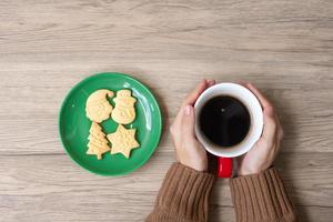 allegro Natale con donna mano Tenere caffè tazza e fatti in casa biscotto su tavolo. natale vigilia, festa, vacanza e contento nuovo anno concetto foto