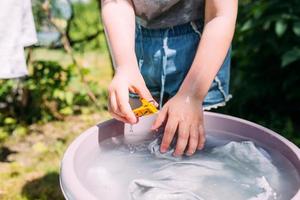 la bambina in età prescolare aiuta con il bucato. il bambino lava i vestiti in giardino foto