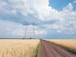 intermedio acciaio alta tensione Torre su un' campo con un' sporco strada. foto