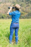 donna indossare cappello e hold binoculare nel erba campo foto