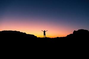 contento festeggiare vincente successo donna a tramonto o Alba in piedi euforico con braccia sollevato su nel celebrazione di avendo raggiunto montagna superiore vertice obbiettivo durante escursioni a piedi viaggio trekking foto