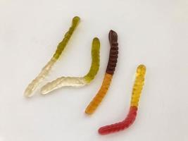 marmellata vermi. gelatinoso vermi, multicolore. bianco-verde e giallo-marrone verme strisciare insieme su un' bianca Opaco sfondo foto