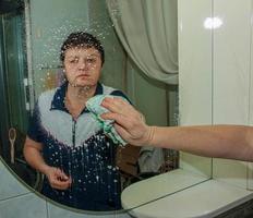 un' donna pulisce un' specchio con un' tovagliolo a partire dal sporco e placca a partire dal acqua a casa foto