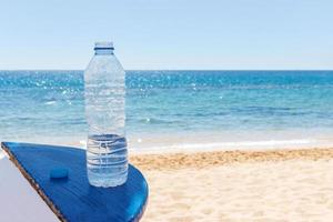 bottiglia di acqua su spiaggia tavolo sotto Aperto cielo su sfondo di mare foto