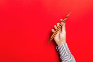 ritagliata Immagine di maschio mano Tenere bastoncini su rosso sfondo. asiatico cibo concetto con copia spazio foto