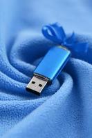 brillante blu USB veloce memoria carta con un' blu arco bugie su un' coperta di morbido e peloso leggero blu vello tessuto con un' lotto di sollievo pieghe. memoria Conservazione dispositivo nel Da donna design foto