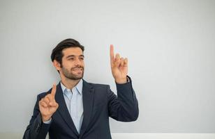 ritratto di sorridente giovane caucasico uomo d'affari indossare buio completo da uomo e presentazione copia spazio su il suo puntamento dito vicino con calcestruzzo parete. foto