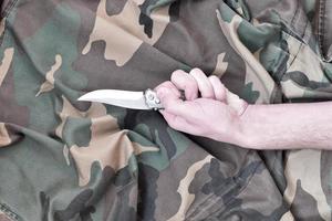 mano con piccolo coltello su camuffare tessuto sfondo. il concetto di utilizzando un' coltello nel mischia tattica tra il soldati foto