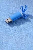 brillante blu USB veloce memoria carta con un' blu arco bugie su un' coperta di morbido e peloso leggero blu vello tessuto. classico femmina regalo design per un' memoria carta foto