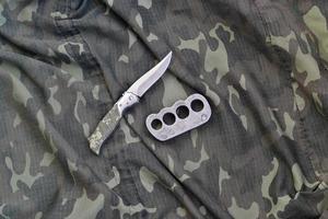 coltello e ottone nocche su un' camuffare Abiti sfondo. utensili per difesa personale o colpevole attacchi foto