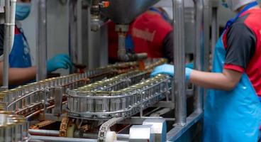 in scatola pesce fabbrica. cibo industria. sardine nel rosso pomodoro salsa nel in scatola lattine su trasportatore cintura a cibo fabbrica. sfocatura lavoratori Lavorando nel cibo in lavorazione produzione linea. cibo produzione industria. foto